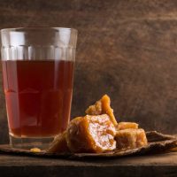 pieces of jaggery or unrefined sugar or palm sugar with a glass of tea, traditional sweetener in southeast asia with a hot drink on wooden surface, moody concept