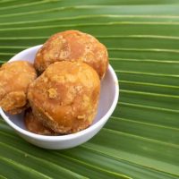 Closeup of Organic Palm Jaggery or Gur in a White Bowl Isolated on a Palm Leaf with Selective Focus and Copy Space.